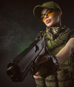 girl in military special clothes posing with a gun in his hands on a dark background in the haze