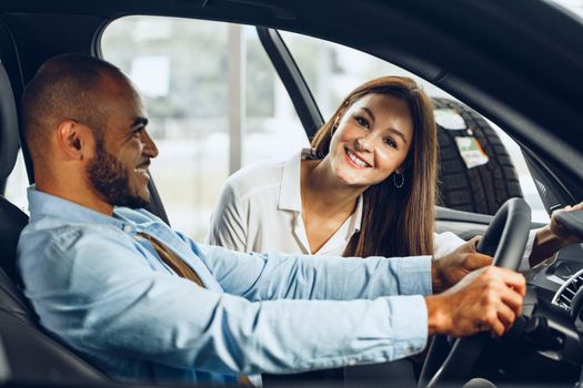 Young woman salesperson in car showroom showing a car to her male client close up