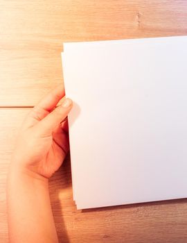 Hand holding sheets of paper on a wooden background