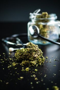 the Dry medical cannabis in a jar with a stethoscope on a black background