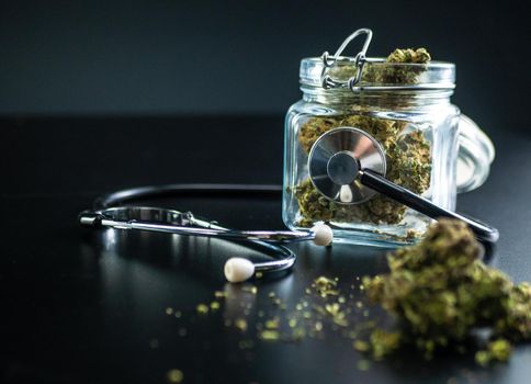 the Dry medical cannabis in a jar with a stethoscope on a black background