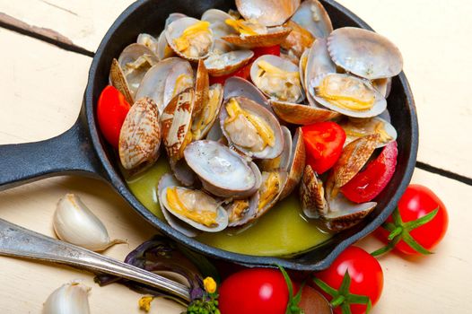 fresh clams stewed on an iron skillet over wite rustic wood table 