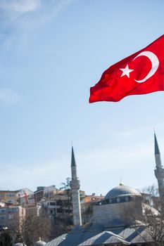 Turkish national flag hang on a pole on a rope with a minaret behind