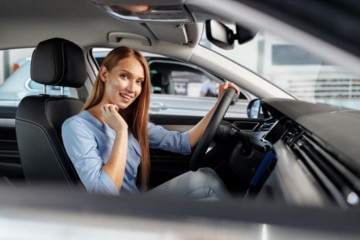 Happy woman new car owner sitting in driver seat and looking around