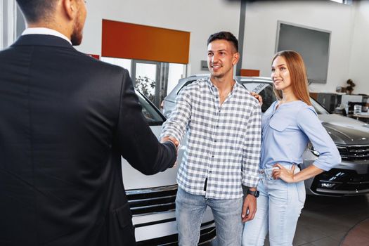 Cherrful young couple at the dealership buying a new car indoors