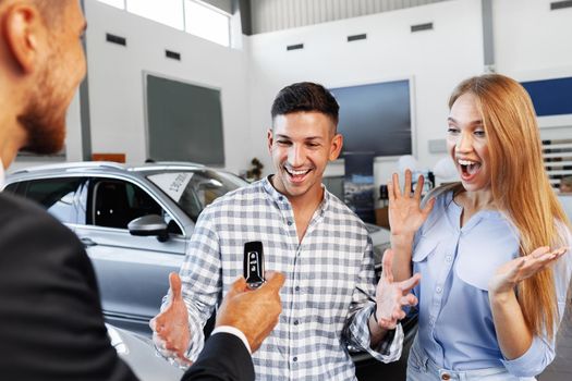 Cherrful young couple at the dealership buying a new car indoors