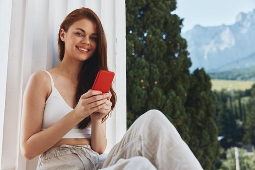 cheerful woman sitting on the balcony with phone beautiful mountain view summer Relaxation concept. High quality photo