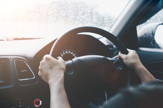 Hand of person on steering wheel drive a car with sunlight background.