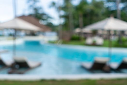 Background of a blurry resort and hotel with a swimming pool and a beach chair.