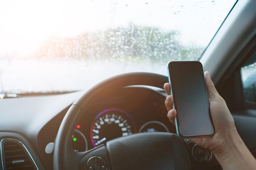 Hand of woman on steering wheel drive a car while using smartphone sunlight background.