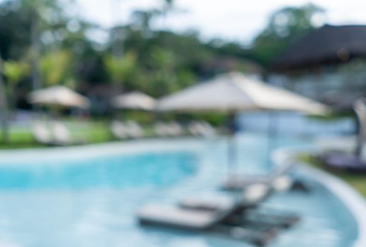 Background of a blurry resort and hotel with a swimming pool and a beach chair.