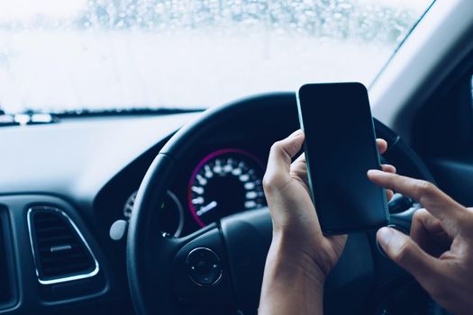 Hand of woman on steering wheel drive a car while using smartphone sunlight background.