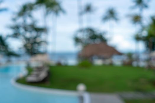 Background of a blurry resort and hotel with a swimming pool and a beach chair.