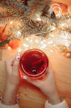 A glass of mulled wine held in their hands against a backdrop of garlands . High quality photo