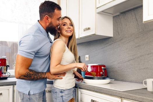 Young man and woman cooking food in kitchen together, happy couple preparing food at home