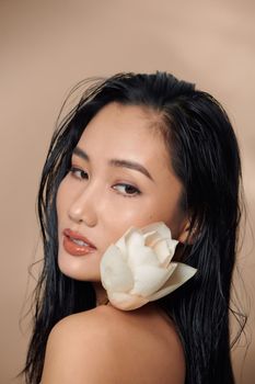 Woman got dark tan skin with long hair and holding flowers on beige background in white cropped top 