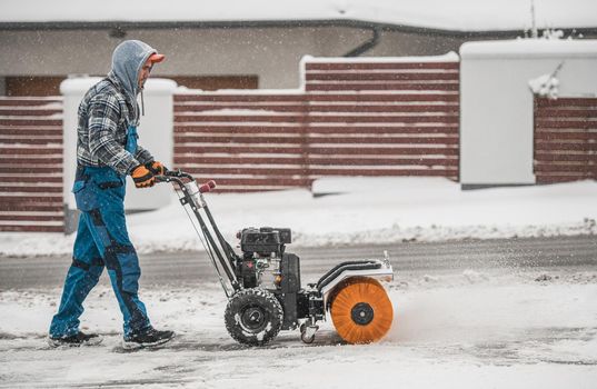 Caucasian Men Cleaning Driveway and Removing Fresh Fallen Snow Using Powerful Gasoline Brush Broom.