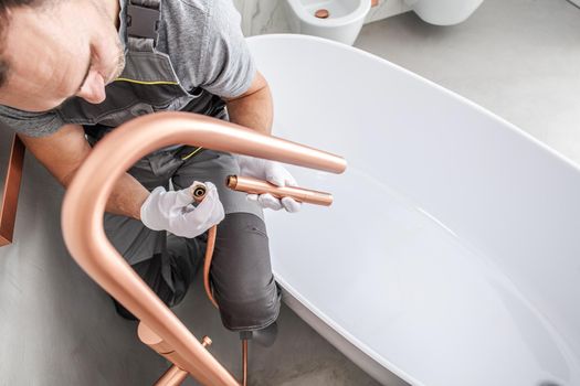 Plumber Connecting Pipes And Attaching Faucet Parts To Finish Installation Of Bathtub.