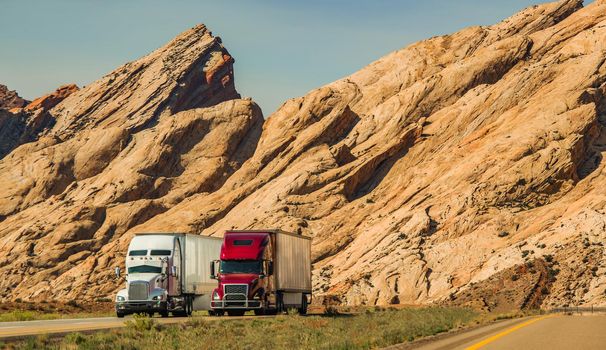 Two Speeding Semi Trucks on Interstate 70 Highway in Scenic Utah Landscape. Heavy Duty American Transportation Industry Theme.