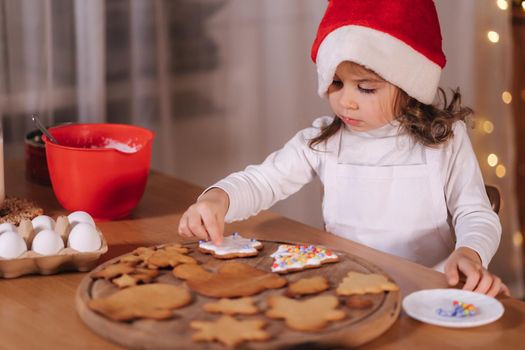 Home bakery, cooking traditional festive sweets. Little girl in red santa hat preparing for making gingerbread dough on wooden table. New Year celebration traditions. Christmas mood.
