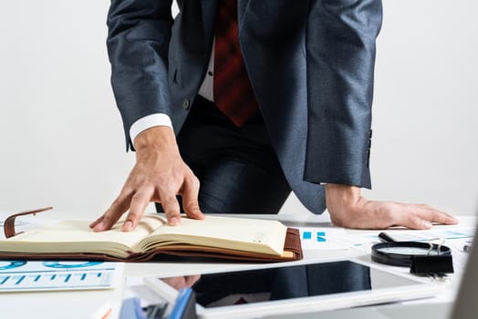 Businessman analyzing financial documents at office desk. Financial expertise and consulting. Manager in suit and tie planning day with personal organizer. Time management and work organization.