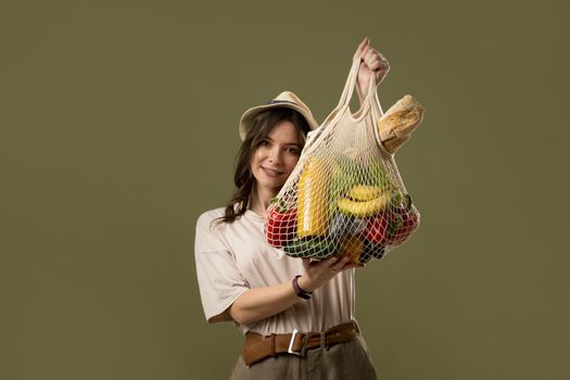 Portrait of smiling young woman in oversize t-shirt holding reusable string bag with groceries. Reusable eco bag for shopping. Zero waste, plastic free concept. Eco lifestyle. Eco shopping