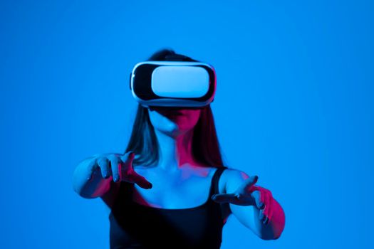 Cheerful girl with hands up wearing the virtual reality goggles and playing a games in neon light. Future technology concept. Metaverse