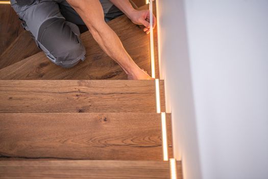 Professional Caucasian Worker Finishing LED Residential Wooden Stairs Lights Installation. Modern Home Illumination Technologies.