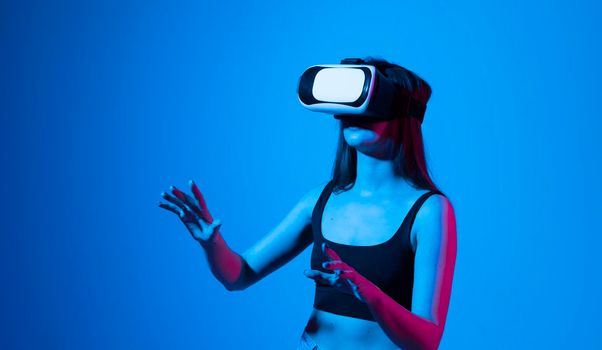Woman with glasses of virtual reality in a neon light. Future technology concept. Young woman touching air while wearing VR glasses