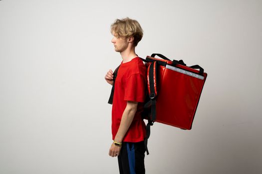 Young delivery employee man in red tshirt uniform with a thermal food bag backpack works as a courier in a food delivery service