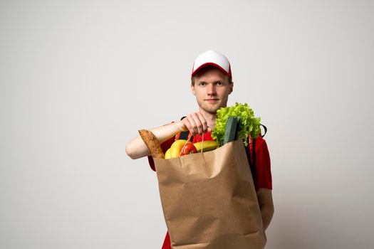 Delivery man employee in red cap and t-shirt uniform hold craft paper packet with food isolated on white background studio