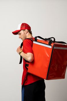 Fast Food Delivery Service Cocnept. Portrait of smiling male courier wearing red uniform holding red thermo backpack bag with a food