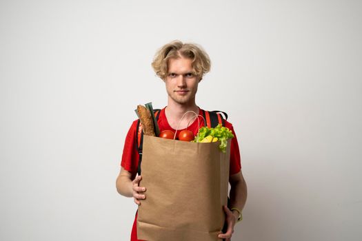 Delivery man employee in red t-shirt uniform hold craft paper packet with food isolated on white background studio