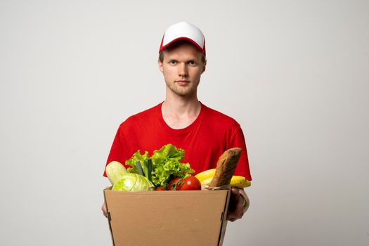 Delivery man in red uniform holds craft paper packet with food isolated on white background, studio portrait. Service concept