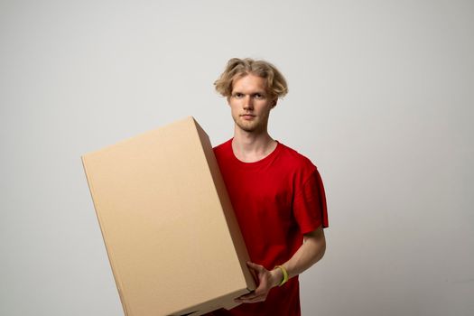 Delivery Service Concept. Male worker in red uniform holding cardboard box isolated over white studio background