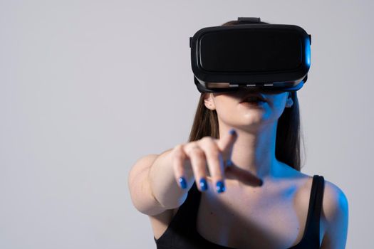 Brunette woman in a black t-shirt and VR headset looking up and trying to touch objects in virtual reality. VR is a technology that simulates a physical presence and to interact with environment