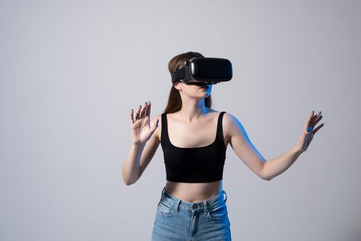 Close up of young woman stands in studio wearing VR glasses and swiping scrolling zooming with hands in a virtual space while interacting with a objects in a social networks