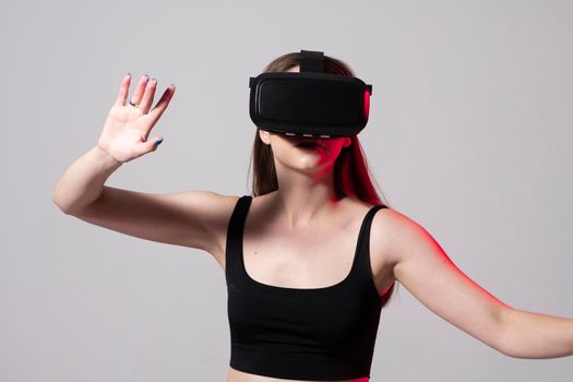 Young woman working in VR goggles on a grey background. Modern architect using virtual reality glasses at workplace. Designer working in augmented reality vr studio