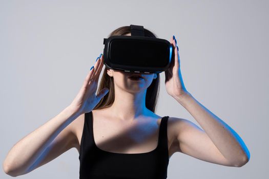 Business woman wearing VR goggles and interacts with metaverse using swipe and stretching gestures. Woman using virtual reality glasses in a studio