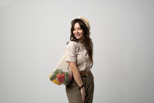 Woman in a beige t-shirt and a hat holding mesh shopping bag with groceries. Conscious consumption. Eco trend. Zero waste concept. Girl carry bag shopper