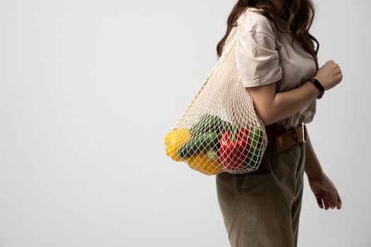 Reusable eco bag for shopping. String shopping bag with fruits and vegetables in the hands of a young woman. Zero waste, plastic free concept. Eco lifestyle. Eco shopping