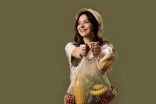 Eco bag string bag with fruits, vegetables, juice and bread in a hands of a brunette girl in a beige suit and a hat. Eco friendly concept. Fashion photography. Zero waste concept