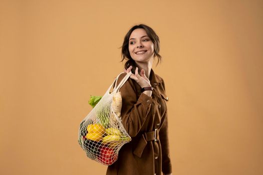 Zero waste concept. Young brunet woman holding reusable cotton shopping mesh bag with groceries from a market. Concept of no plastic. Zero waste, plastic free. Sustainable lifestyle