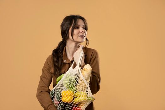 Reusable eco bag for shopping. String shopping bag with fruits and vegetables in the hands of a young woman. Zero waste, plastic free concept. Eco lifestyle. Eco shopping