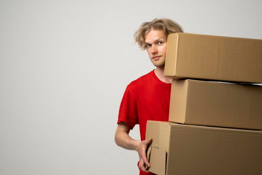 Courier in a red uniform holding a stack of cardboard boxes. Delivery man delivering postal packages over white studio background