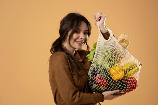 Zero waste concept. Young brunet woman holding reusable cotton shopping mesh bag with groceries from a market. Concept of no plastic. Zero waste, plastic free. Sustainable lifestyle