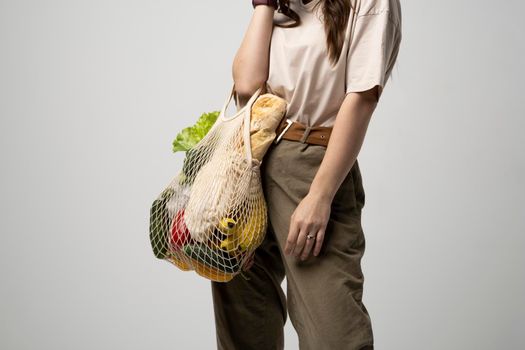 Portrait of smiling young woman in oversize t-shirt holding reusable string bag with groceries. Reusable eco bag for shopping. Zero waste, plastic free concept. Eco lifestyle. Eco shopping