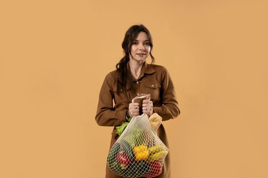 Zero waste concept. Young brunet woman holding reusable cotton shopping mesh bag with groceries from a market. Concept of no plastic. Zero waste, plastic free. Sustainable lifestyle