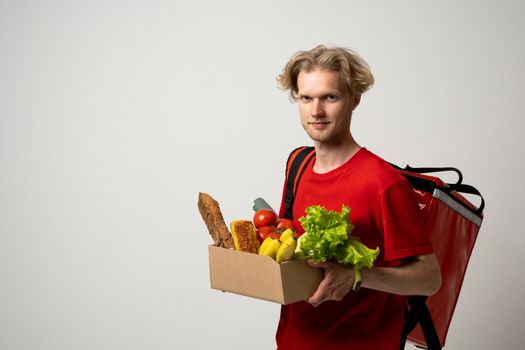 Courier man in red uniform with a thermal bag backpack hold craft paper bag takeaway with food products isolated on white background studio. Delivery service from shop restaurant to home