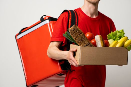 Delivery Concept. Handsome delivery man in a red uniform carrying paper box of grocery food and drink from store isolated on white studio background. Copy Space